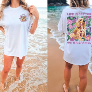 Op de afbeelding: Wit T-shirt met een afbeelding van een spaniel-hond omringd door bloemen en de tekst "Life is better with a spaniel".