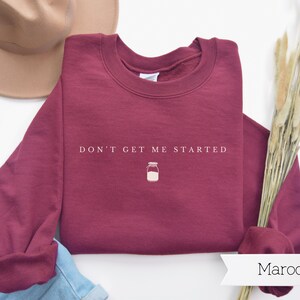 May include: Maroon sweatshirt with the text "Don't get me started" and a small illustration of a jar.