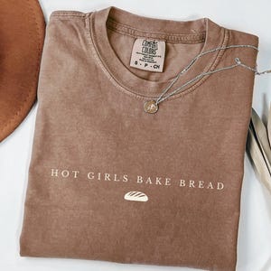 May include: A brown t-shirt with the text "HOT GIRLS BAKE BREAD" and a small bread graphic printed on the front.