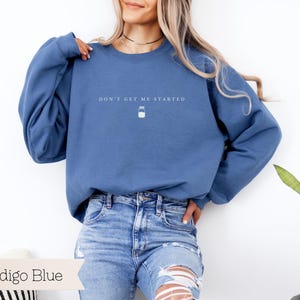 May include: A blue sweatshirt with the text "Don't get me started" and a small jar icon. The model is wearing the sweatshirt with blue jeans.