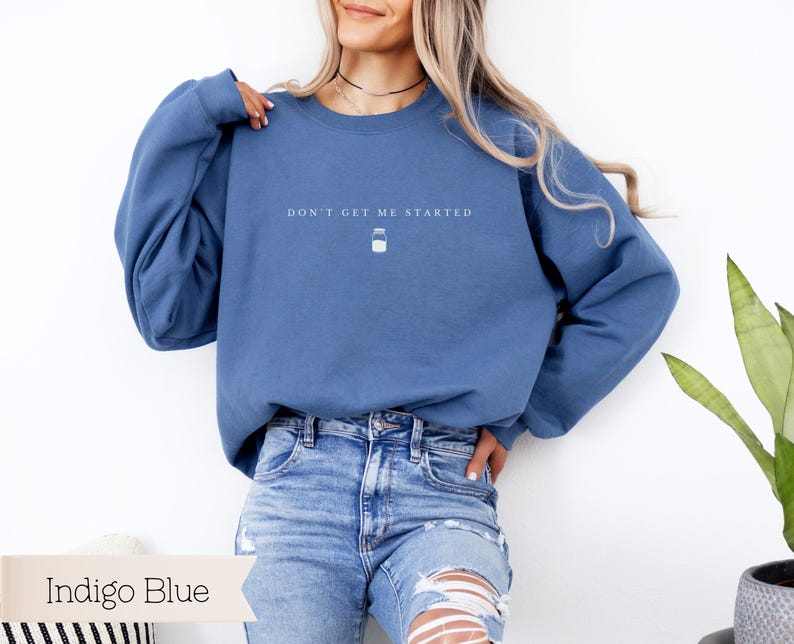 May include: A blue sweatshirt with the text "Don't get me started" and a small jar icon. The model is wearing the sweatshirt with blue jeans.