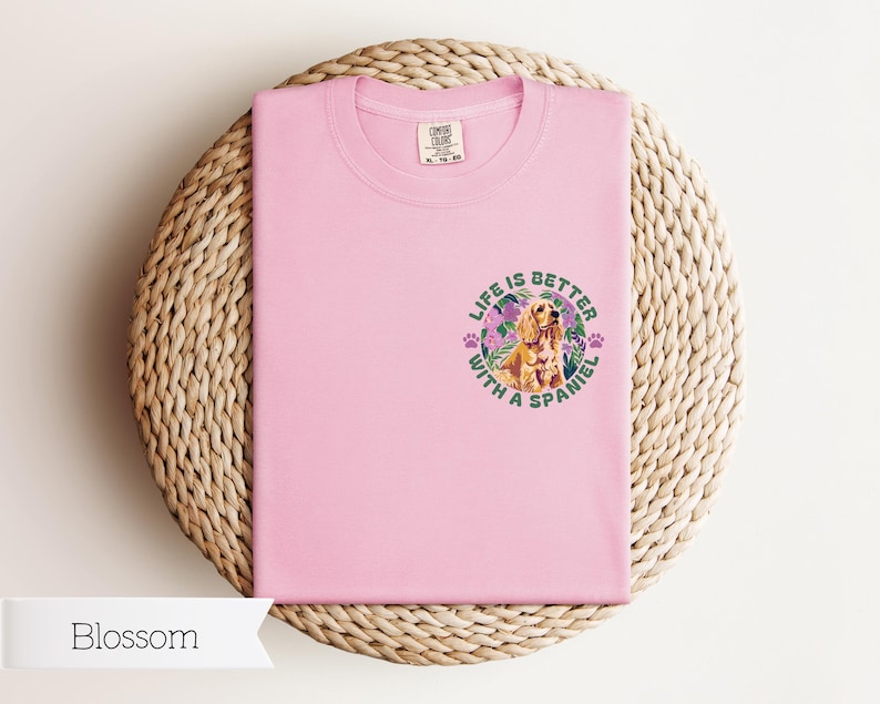 Op de afbeelding: Roze T-shirt met een afbeelding van een spaniel-hond met bloemen en de tekst "Life is better with a spaniel".