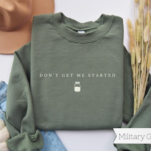 May include: A military green sweatshirt with the text "Don't get me started" and a small illustration of a milk jug.