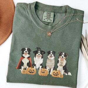 May include: Green t-shirt with a graphic of four dogs dressed in Halloween costumes. The dogs are wearing a cape, a witch's hat, a mummy costume, and a "Trick or Treat" bag. The dogs are surrounded by pumpkins.