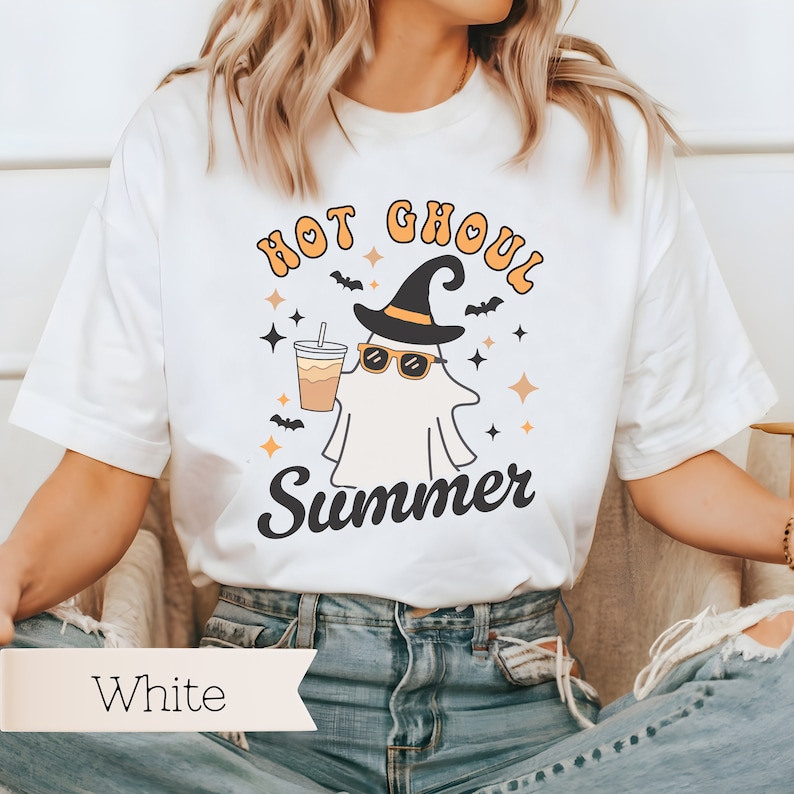 May include: White t-shirt with a graphic of a ghost wearing a witch hat and sunglasses, holding a cup of coffee. The text "Hot Ghoul Summer" is printed on the shirt.
