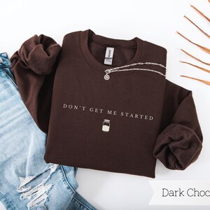 May include: A dark chocolate brown sweatshirt with the text "Don't Get Me Started" and a small milk jar graphic.