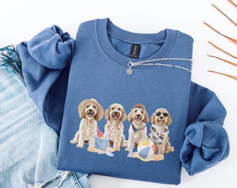 May include: A blue sweatshirt with a graphic of four doodle dogs wearing sunglasses and holding beach items. The dogs are wearing a variety of outfits, including a red bandana, a blue and white striped shirt, and a yellow and white striped shirt. The sweatshirt has a silver chain necklace with a small pendant.