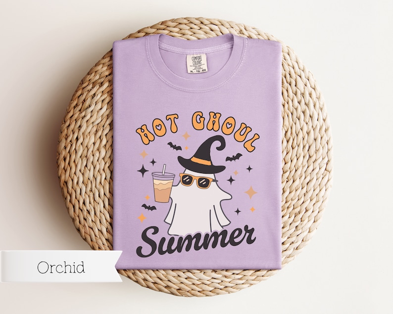 May include: A purple t-shirt with a ghost wearing a witch hat and sunglasses holding a cup of coffee. The text on the shirt reads "Hot Ghoul Summer".