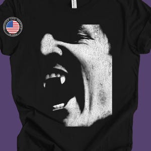 May include: Black and white graphic t-shirt featuring a close-up of a vampire's face with fangs and a distressed, textured background.