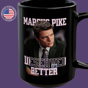 May include: Black coffee mug with a white image of Marcus Pike from the TV show "White Collar". The text "Marcus Pike" is in white letters at the top of the mug. Below the image is the text "Deserved Better" in pink letters.