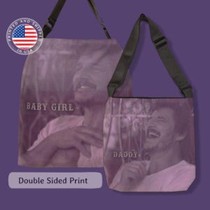 May include: Two purple shoulder bags with a double-sided print. One bag features the text "BABY GIRL", and the other says "DADDY". Both bags display a black and white image of a person. The bags have black straps and are printed and shipped in the USA.