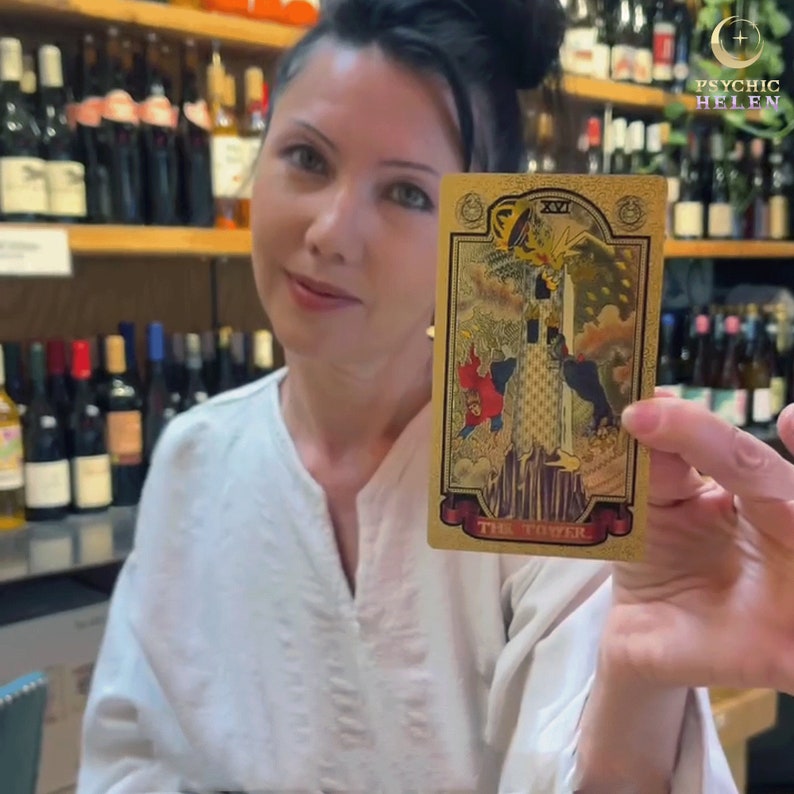 Pu&ograve; includere: Una carta dei tarocchi dorata con l'immagine di una torre, persone che cadono e la scritta "THE TOWER". La carta &egrave; tenuta da una donna con una camicia bianca. Lo sfondo include scaffali di bottiglie di vino.