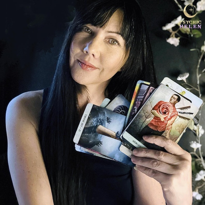 May include: A woman holds a spread of tarot cards, including the "VII - The Chariot" card. The cards feature colorful illustrations and intricate designs.
