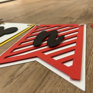 May include: A decorative banner with pennant flags in red, yellow, and white. The red flag features a diagonal striped design and a black letter "n". A black Mickey Mouse head is visible on a white flag.