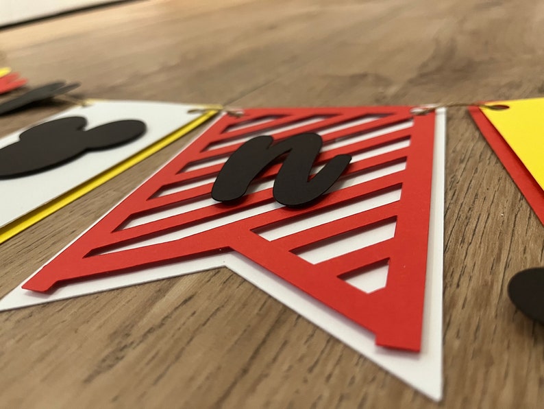 May include: A decorative banner with pennant flags in red, yellow, and white. The red flag features a diagonal striped design and a black letter "n". A black Mickey Mouse head is visible on a white flag.