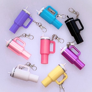 May include: Ten colorful keychain bottle openers with different designs. Each bottle opener has a metal ring and a small loop for attaching to a keychain. The bottle openers are in various colors, including pink, blue, black, white, and purple.