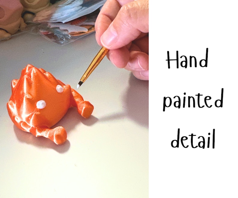 K&ouml;nnte beinhalten: Eine Hand bemalt Details auf einer kleinen, orangefarbenen 3D-gedruckten Krabbenfigur mit wei&szlig;en Augen. Handbemalte Details.