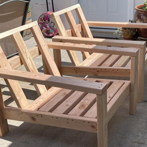 Puede incluir: Dos sillas de madera sin terminar con respaldos y asientos de listones. Las sillas son de madera natural y tienen un aspecto r&uacute;stico.