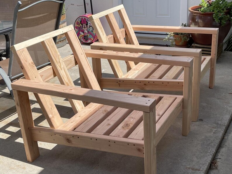 Puede incluir: Dos sillas de madera sin terminar con respaldos y asientos de listones. Las sillas son de madera natural y tienen un aspecto r&uacute;stico.