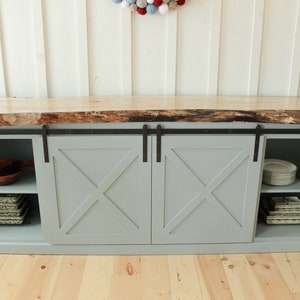 May include: A grey cabinet with two sliding barn doors. The doors have a criss-cross design and are made of wood. The cabinet has a live edge wood countertop and shelves inside.