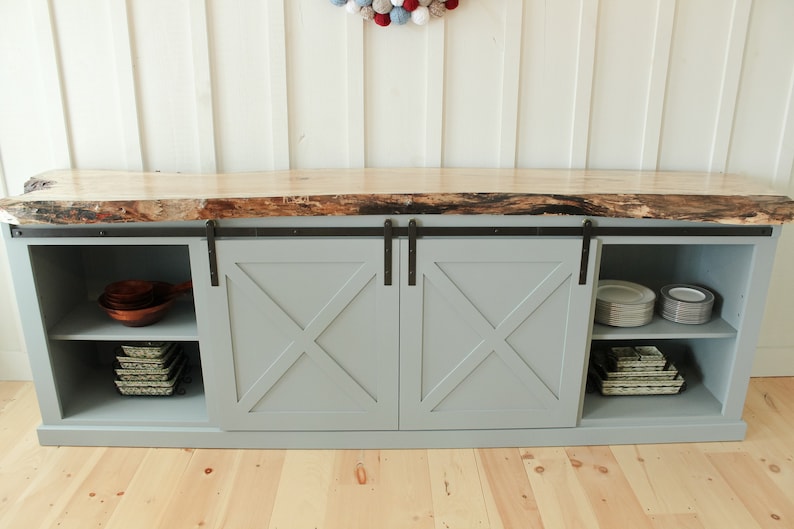 May include: A grey cabinet with two sliding barn doors. The doors have a criss-cross design and are made of wood. The cabinet has a live edge wood countertop and shelves inside.