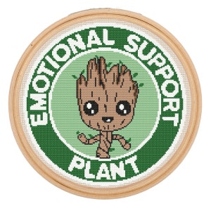 Könnte beinhalten: Ein grüner und weißer Stickrahmen mit grünem Hintergrund und weißem Text, der "Emotional Support Plant" lautet. In der Mitte des Rahmens befindet sich ein Cartoon-Bild eines braunen, humanoiden Baumes mit einem lächelnden Gesicht.
