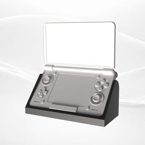 Könnte beinhalten: Eine silberne Handheld-Spielkonsole mit schwarzem Sockel. Die Konsole hat zwei Bildschirme, ein Steuerkreuz, Tasten und einen Joystick. Der obere Bildschirm ist geöffnet, und der untere Bildschirm ist sichtbar. Das Design ist schlicht und modern.