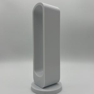 Pu&ograve; includere: Un oggetto grigio chiaro, orientato verticalmente, di forma rettangolare cava con angoli superiori arrotondati, montato su una base circolare. La struttura presenta una cornice continua e liscia con un'ampia apertura allungata al centro.