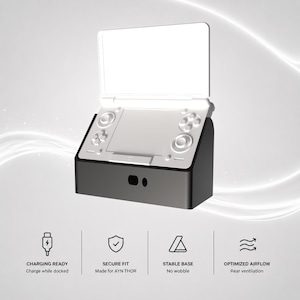 Op de afbeelding: Een zwart dockingstation voor een draagbare spelconsole, voorzien van een gevormde houder voor een veilige pasvorm, een stabiele basis en ventilatie aan de achterzijde. Tekst: CHARGING READY, SECURE FIT, Made for AYN THOR, STABLE BASE, No wobble, OPTIMIZED AIRFLOW.