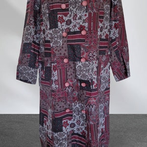 May include: A long-sleeved, double-breasted coat with a patchwork design in shades of grey, black, and burgundy. The coat has pink buttons and a paisley pattern.