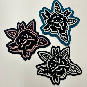 May include: Three felt patches with black embroidered roses. The roses are outlined in white, pink, and teal.