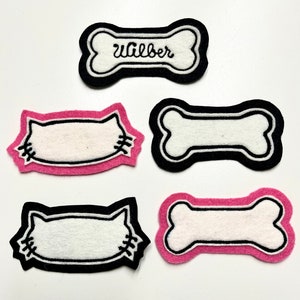 May include: Five felt bone-shaped patches with white centers and black outlines. Two patches are pink with black stitching. Two patches are black with white stitching. One patch is black with white stitching and the name "Gilber" embroidered in black thread.
