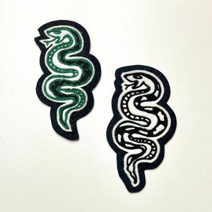 May include: Two embroidered iron-on patches featuring a snake design. One patch is green on a black background, and the other is black on a white background.