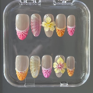 Peut inclure: Un ensemble de dix faux ongles avec différents motifs. Les ongles sont nus avec une pointe blanche et présentent des accents roses, oranges et jaunes. Certains ongles ont un motif de fleur, tandis que d'autres ont un motif de nœud.