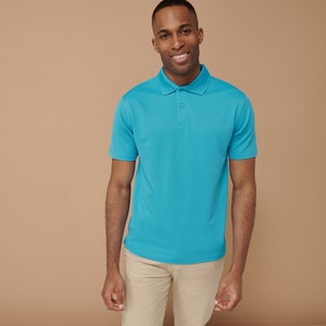 K&ouml;nnte beinhalten: Ein Mann tr&auml;gt ein hellblaues Poloshirt und eine Khakihose. Er l&auml;chelt und schaut in die Kamera.