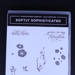 Peut inclure: Un ensemble de sept tampons en photopolymère avec des motifs floraux et des sentiments. Les tampons sont emballés dans un étui en plastique transparent avec le titre "Softly Sophisticated" et le texte "hello there", "you're in my thoughts", et "I really appreciate you".