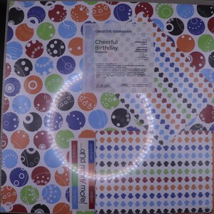 Puede incluir: Un paquete de papel con patrones coloridos sobre un fondo blanco y círculos de diferentes colores y diseños. El papel está etiquetado como "Cheerful Birthday Additions" e incluye el texto "...and many more!" y "happy day to you!"