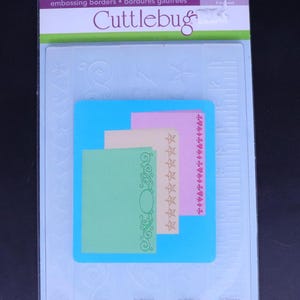 Könnte beinhalten: Eine Packung Cuttlebug Präge-Ränder mit fünf verschiedenen Designs. Die Packung enthält ein Muster jedes Designs, das auf farbigem Papier geprägt ist. Die Packung ist blau und weiß mit dem Text "Measure by Measure" und "Embossing Borders - Bordures Gauffrées" bedruckt.