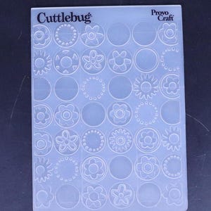 May include: A clear plastic sheet with a grid of 36 circles, each containing a different floral design. The sheet is labelled "Cutterbug" and "Provo Craft".