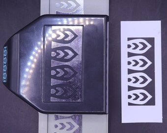 May include: A black and grey paper punch with a silver leaf design. The punch is open and a sample of the punched design is on a white piece of paper.