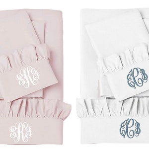 May include: Two sets of bed linen with ruffled edges. One set is pink with white embroidered initials, the other is white with blue embroidered initials.