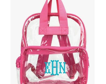 May include: A clear backpack with pink trim, straps, and a top handle. The front pocket features the embroidered initials "EHN" in a teal color. The backpack has a zippered front pocket and adjustable shoulder straps.