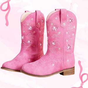 May include: A pair of pink cowboy boots with star and floral embroidery. The boots have a classic western design with a pointed toe and a low heel. The boots are made of a soft, suede-like material.