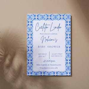 Peut inclure: Une invitation de fête prénatale blanche avec une bordure à motifs bleus et blancs. Le texte indique "Cielito Linda" et "Veuillez vous joindre à nous pour célébrer la fête prénatale de Nohemi". L'invitation comprend la date, l'heure et le lieu de l'événement. Elle comprend également le texte "Liste de naissance sur Amazon.com" et "Apportez des couches pour participer à la tombola".
