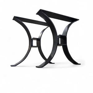 May include: Two black metal table legs with a curved, modern design. Each leg features a rectangular top and base, connected by a curved support with a square accent. The legs are designed for a table and are suitable for various interior styles.
