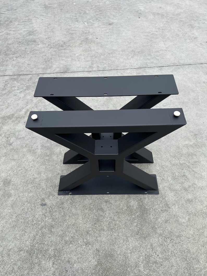 May include: Black metal table base with an X-shaped design. The base has two flat top plates and a lower support structure.