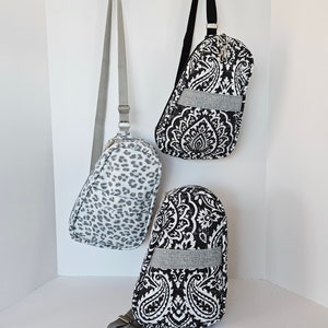 May include: Three black and white patterned crossbody bags hanging on hooks. The bags have a gray strap and a gray band across the front.