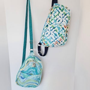 May include: Two teal and blue patterned crossbody bags hanging on hooks. The bag on the left has a wavy pattern and the bag on the right has a geometric pattern.