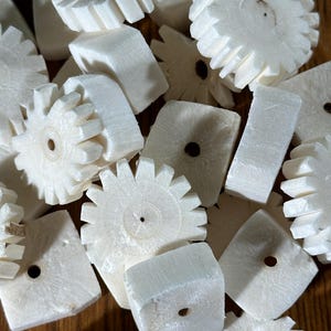 May include: A collection of small, off-white wooden gears and square blocks with a central hole. The gears have a star-like design, and the blocks are rectangular. The items are scattered on a wooden surface.