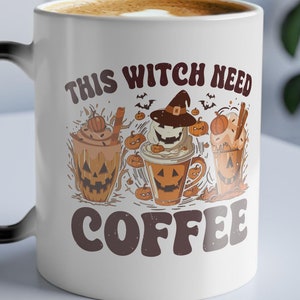 Op de afbeelding: Witte keramische koffiemok met een zwart handvat, met de tekst "THIS WITCH NEED COFFEE" in bruin. De mok heeft een Halloween-thema ontwerp met drie koffiekopjes illustraties met pompoengezichten en heksenhoeden.